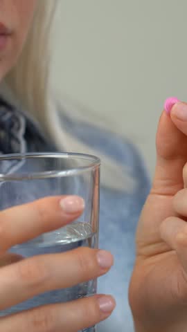 Close up of woman takes pill and drinks with water. Tablets and drugs, medicament, vitamins, contraceptives. Medicine and health care. Vertical shot