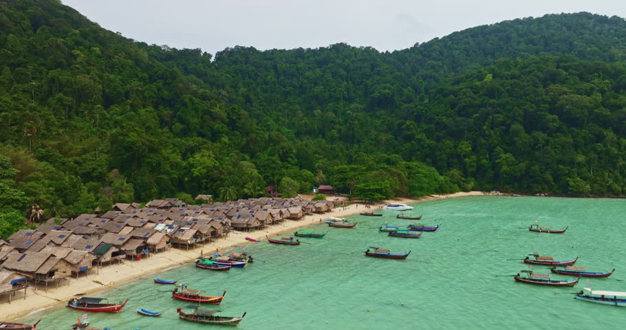  A stunning aerial view of a tropical beach village with rows of small huts along the coastline, Traditional fishing boats are anchored in the turquoise waters at Morgan village. white sandy beach.