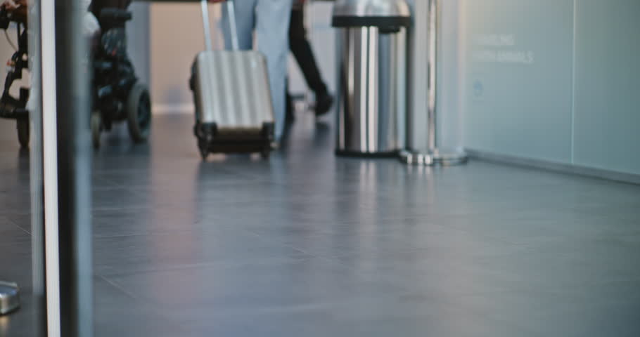 Crowded International Airport Terminal: Knee Level Shot of Diverse People Walking with Luggage for Boarding Plane Flight. Passenger with Disability in Wheelchair. Tourism and Travelling. Slow motion.
