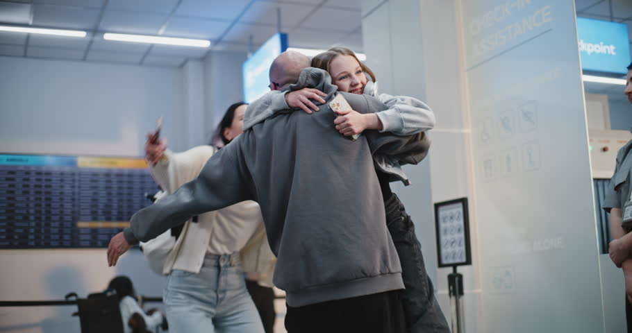 Emotional Family Reunion in Airport Terminal: Happy Man Greeting His Family Back From Vacation Trip, Lifts His Daughter in Arms. Diverse People Walking with Luggage for Boarding Flights. Slow Motion.