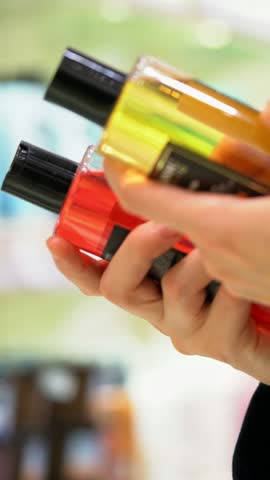 VERTICAL VIDEO A female customer compares two shampoos, reading the labels examines the ingredients for conscious choosing. Close-up of woman's hands holding two bottles in a cosmetic hair care aisle
