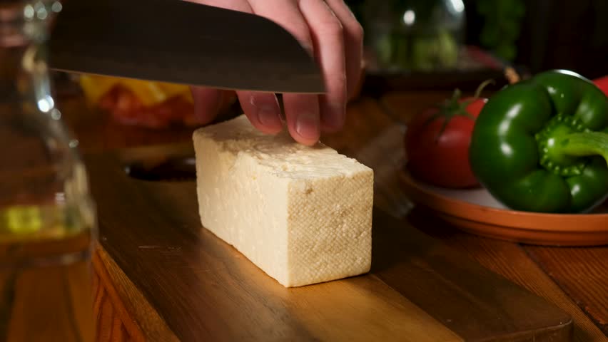 A chef uses a kitchen knife to cut traditional salted feta cheese to add to a vegetable salad. Cutting brine cheese with a knife. Feta cheese. Cheeses that go well with vegetables. Vegetarianism