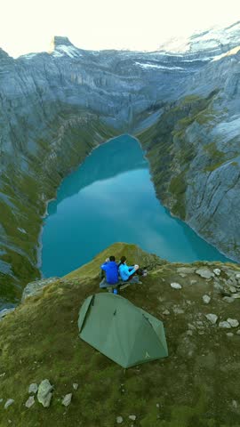 Vertical aerial drone view of Lake Limmernsee in Switzerland. Two people have set up a campsite on a nearby mountain ridge, enjoying the view.