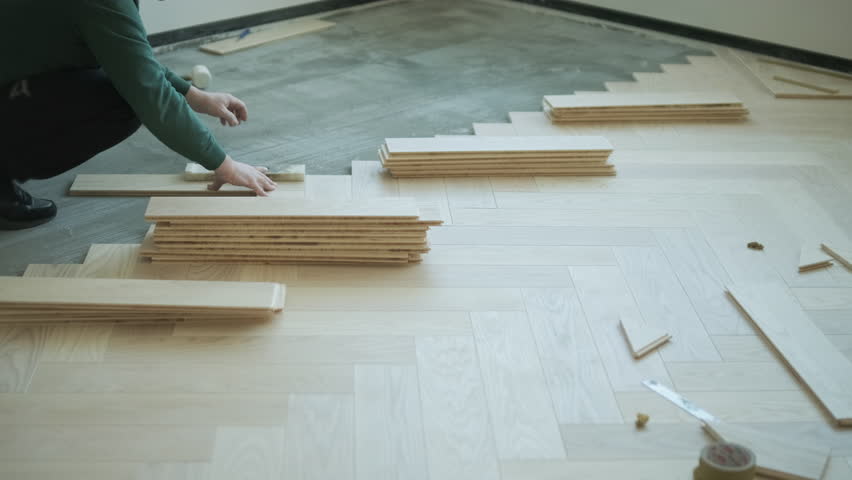 Worker installing wooden flooring with hammer and tapping block
