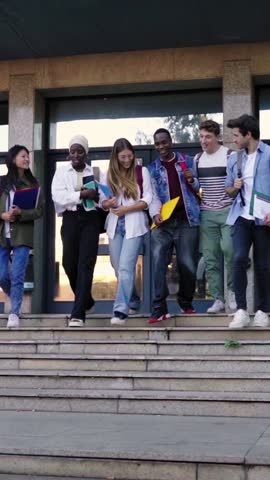 Multicultural group of students walking going out of university, leaving to go home. Front view of classmates outside of the school after class. Vertical video with copy space.