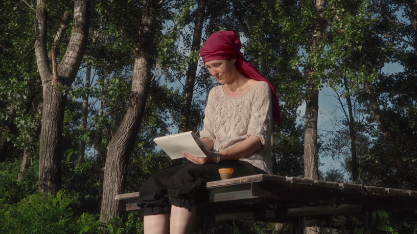 Female painting a landscape in watercolor while sitting on a wooden pier on the bank of a river