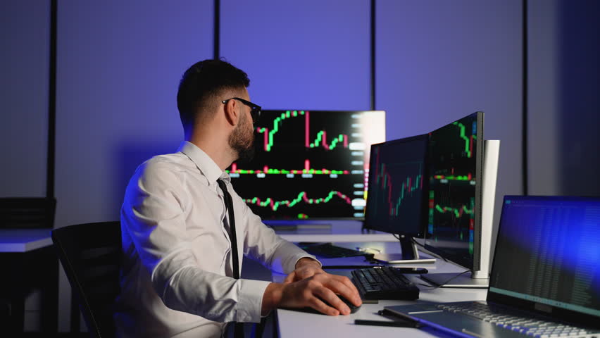 Stock trader analyzing financial charts on multiple screens