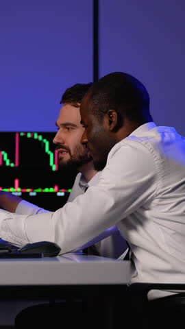 Two brokers analyzing stock market charts on multiple screens