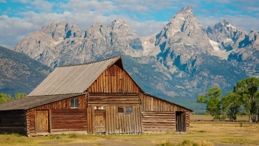 Dramatic low-angle view of a rustic wooden barn, towering mountains in the background, scenic countryside, rural charm, and historic architecture.