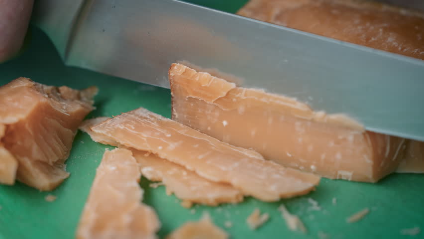 Professional Chef Cutting Extra Hard Cheese: Crumbly Parmesan Slicing Technique with Sharp Kitchen Knife on Green Cutting Board