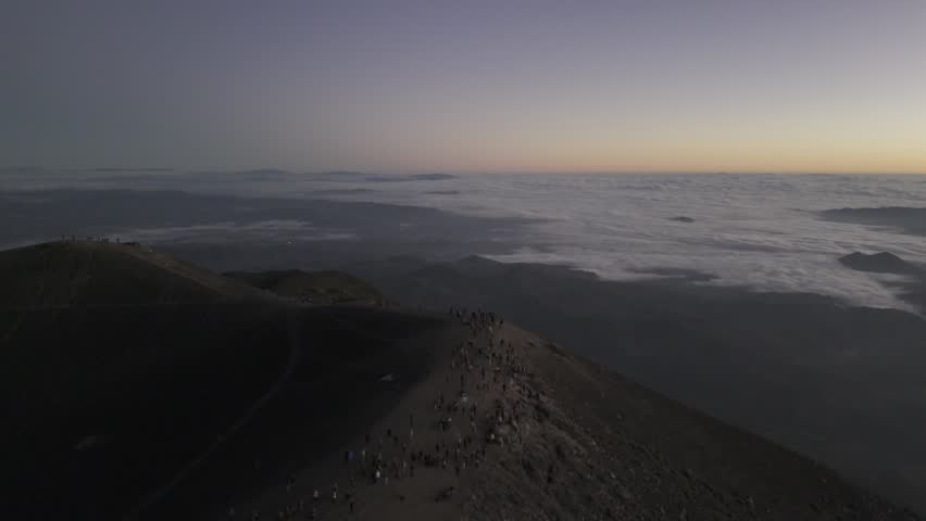 Drone flies backwards over Acatenango with hundreds of hikers at the summit enjoying a sunrise in Guatemala