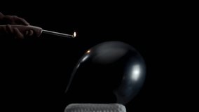 A black balloon lays still against a black background. A hand holding a lighter moves closer and closer, building tension until the balloon pops in a dramatic, slow-motion moment of suspense. - Powered by Shutterstock - Get 15% off with code: PIKWIZARD15