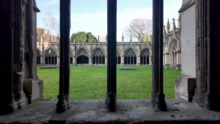 Architectural detail showing stone columns framing the tranquil green courtyard of The Great Cloister at Canterbury Cathedral in England