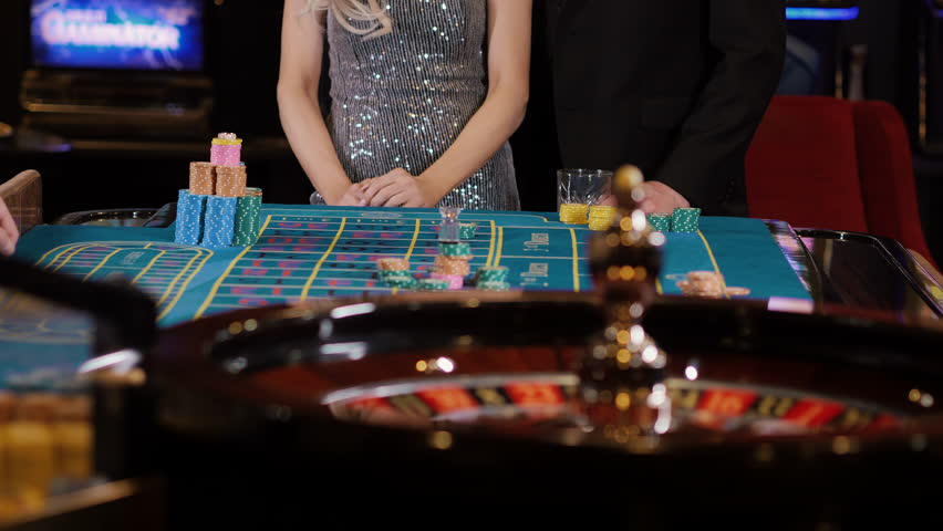Woman gathers casino chips on a roulette table in a luxury casino hall, capturing gambling atmosphere and elegant nightlife in a vibrant casino environment.