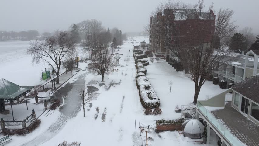 Snow is heavily covering the promenade next to Memphremagog lake in Orford, Quebec, Canada, during a winter blizzard, with a hotel visible on the right