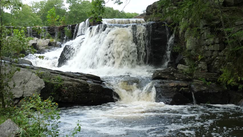 A fast flowing waterfall in a New England Connecticut forest setting featuring rock walls and boulders.