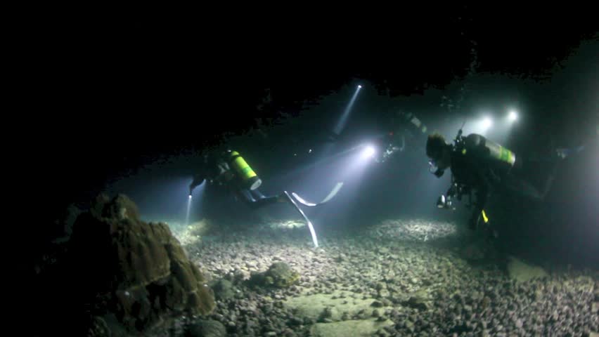 At night, a group of scuba divers use powerful lights to illuminate a rocky reef