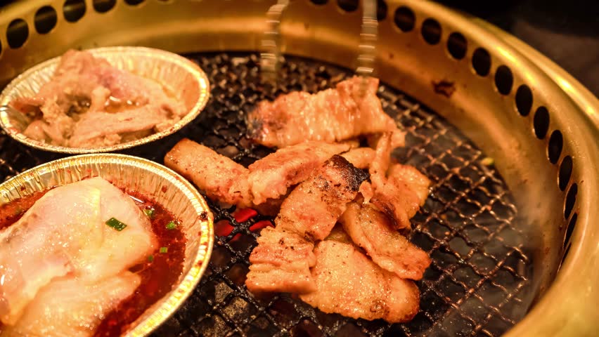 Close-up view of sizzling meat grilling on a Korean BBQ with side dishes in aluminum foil on a grilling pan