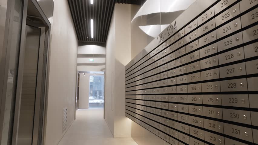 Metallic mailboxes neatly arranged in numbered rows along bright residential corridor, highlighting organized communication infrastructure within modern apartment building