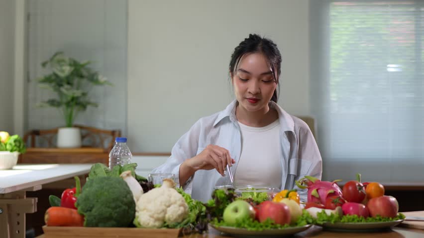 Young woman enjoying nutritious salad with fresh fruits and vegetables, representing healthy eating habits at home kitchen dining table