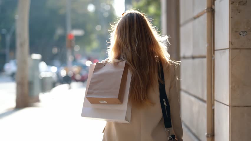 Video of happy smiling woman carrying shopping bags while walking through the city. Looking at camera