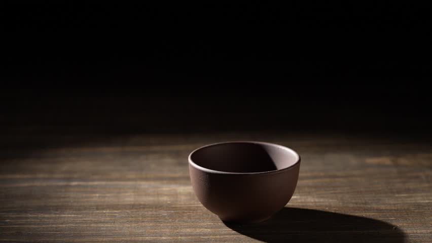Japanese sake from a bottle being poured into ceramic cup on a wooden table, close up, slow motion