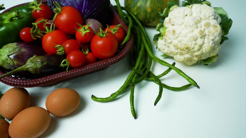 Fresh Vegetables and Eggs on White Surface Footage, A basket filled with fresh vegetables including tomatoes, eggplants, and green beans
