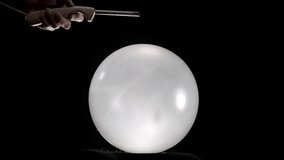 A dramatic scene where a big round white balloon pops as a hand holding a lighter approaches it. The tension builds as the flame nears, culminating in the sudden burst of the balloon. - Powered by Shutterstock - Get 15% off with code: PIKWIZARD15