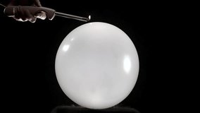 A round balloon pops in slow motion as a hand holding a lighter gets closer. The hand is visible in front of a black background, adding a dramatic effect to the tense moment before the burst. - Powered by Shutterstock - Get 15% off with code: PIKWIZARD15