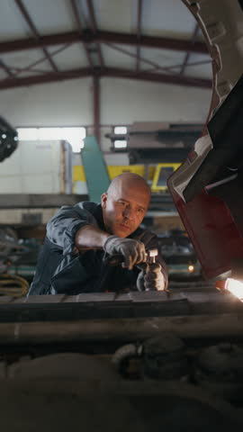 Vertical slowmo shot of skilled middle-aged Caucasian male mechanic wearing cotton gloves using wrench working in garage