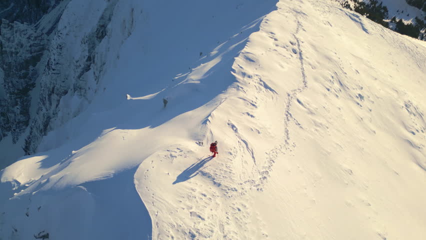 A person in red climbs a steep, snow-covered mountain slope, showcasing their determination and adventurous spirit.