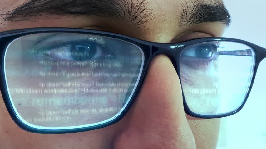 A man working on computer looking at programming code reflecting in his glasses
