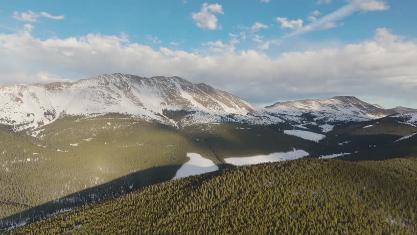 Backward aerial view of pine trees on top of Copper Mountain with cumulus clouds in sky in Colorado, USA.