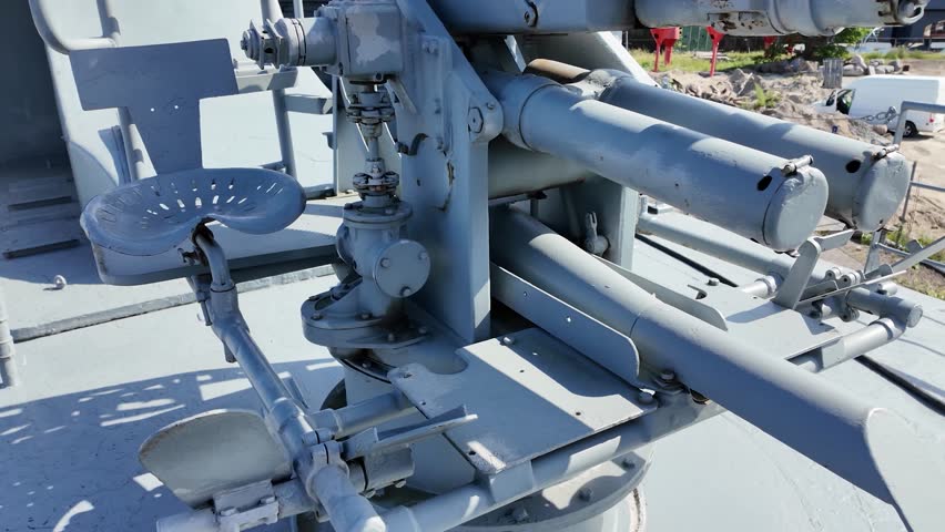 Detailed view of a vintage naval artillery mount with a metal operator seat and mechanical components, displayed on a decommissioned military ship.