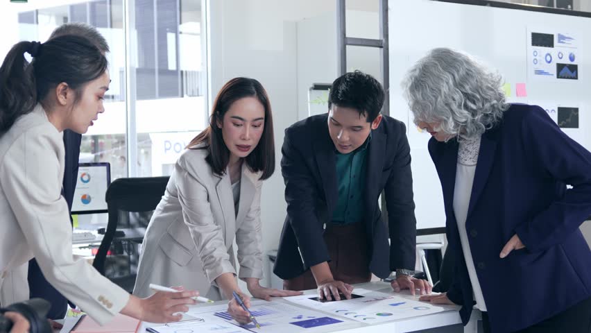 Professional Asian business team analyzing marketing performance data, collaborating over large paper charts during strategic office meeting, discussing growth strategies and innovative solutions - Powered by Shutterstock - Get 15% off with code: PIKWIZARD15