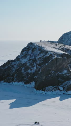 Aerial around view of frozen Lake Baikal, Olkhon Island, Khoboy rock cape. Siberia, Russia. Vertical video
