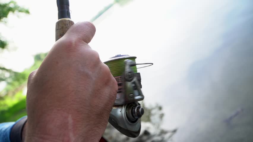 Fishing at a serene lake with a focus on the fishing reel and determination of the angler