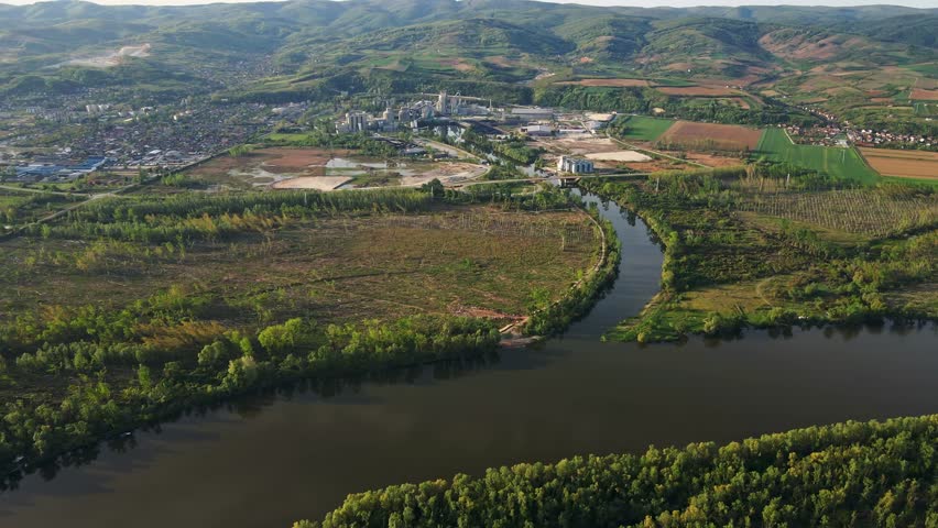 River winding through lush landscape near town with industrial area in the background during sunny day