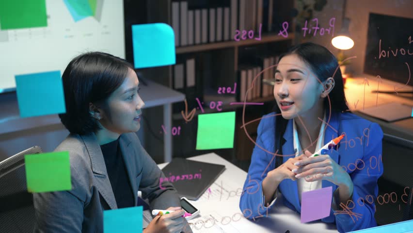 Professional Asian businesswomen collaborating, strategizing with transparent board, colorful sticky notes, marking key points, visualizing business growth and planning