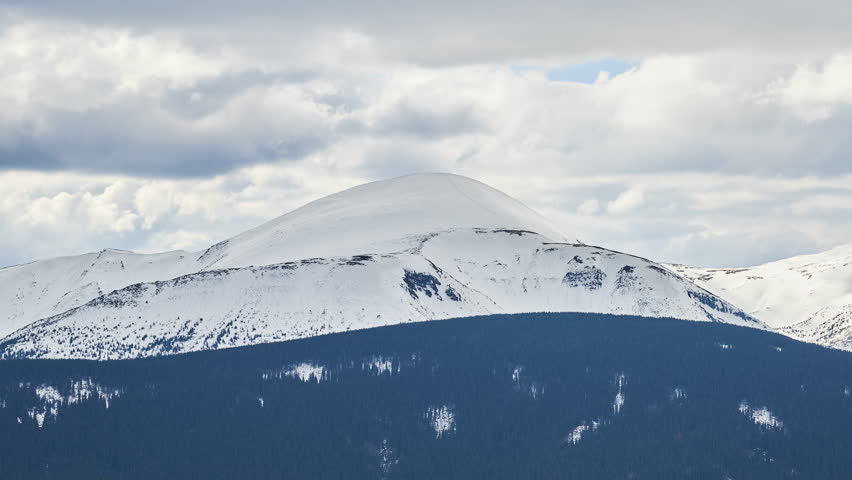 Stunning winter scene showcasing majestic, snow-covered mountain peak under cloudy sky. Mountain
