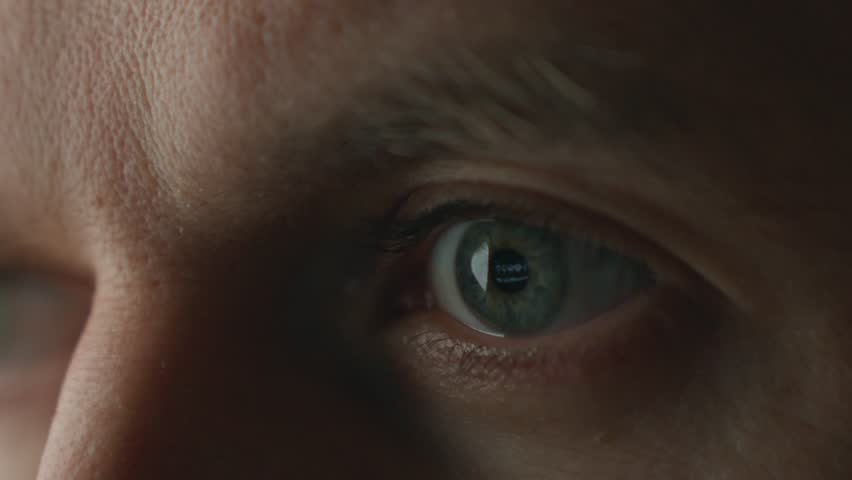 Close-up of human eye watching TV in dark room. Male eye with screen reflection in pupil