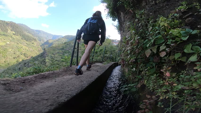 A backpacker ascends a rugged levada trail, walking beside steep cliffs covered in thick vegetation, embracing the island’s wild beauty.