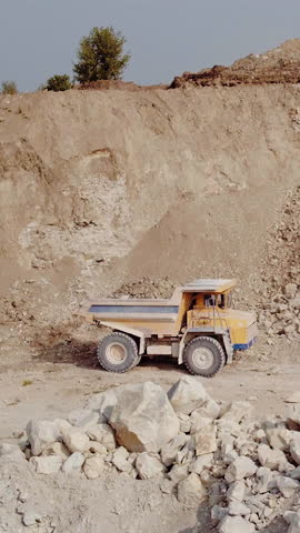 Vertical Format Video of Mining industry concept. Truck is taking ore out of the open pit. Quarry, opencast mining, ore extraction concept. Dump truck loaded with ore and driving through the pit.