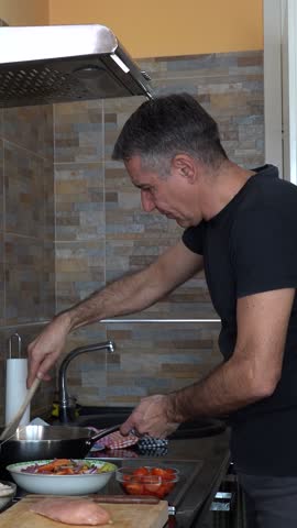 Cheerful Man Cooking at Home While Communicating Over a Digital Tablet. Middle-aged Man using tablet in his kitchen and talks with the person, over the internet, about the cooking process.