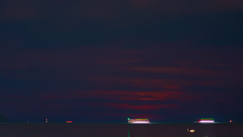 Time lapse A stunning blood moon over the ocean, casting a golden-orange glow across the sky and reflecting on the sea. A small boat and distant lights add depth to the tranquil night scene.