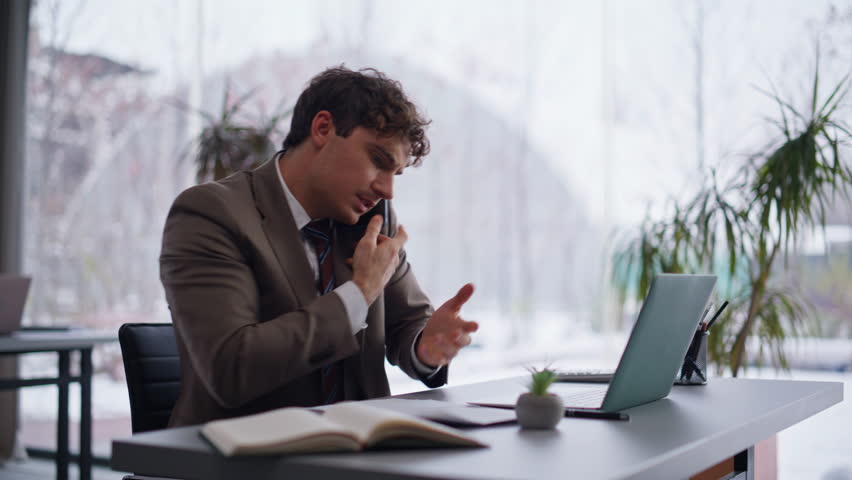Calling businessman feeling nervous discussing document mistake at corporate office closeup. Stressed professional talking cellphone looking papers at modern coworking setting. Man arguing smartphone