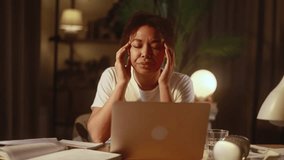 An African American woman works on her laptop in a cozy home setting she rubs her temples and closes her eyes in discomfort suffering from headache and eye strain due to prolonged screen time and work - Powered by Shutterstock - Get 15% off with code: PIKWIZARD15
