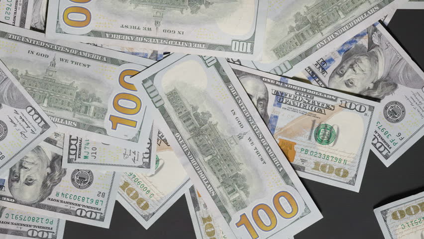 A hand greedily gathers scattered hundred-dollar bills from the table, sweeping them away in a swift motion, symbolizing ambition, greed, or financial dominance, top view