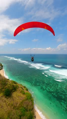 FPV drone shot of paragliders gliding over turquoise ocean and cliffs in Bali, Indonesia