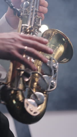 Vertical Video of Saxophone player playing a solo in jazz band, performing on lightened stage. Sax musician player with band at concert. Musical band group playing song, performing on musician stage
